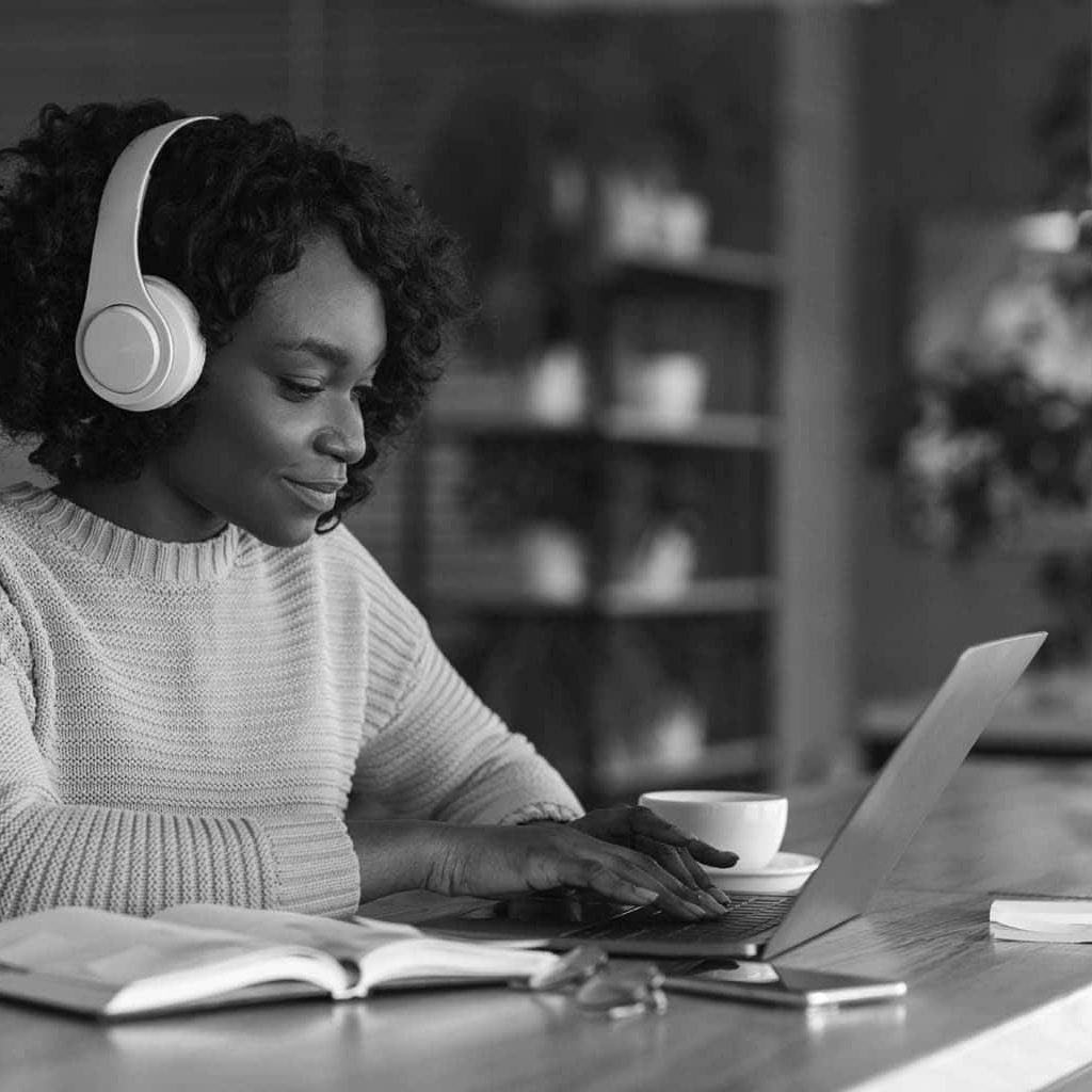 Young afro woman having online training, using laptop and wireless headset at cafe, free space